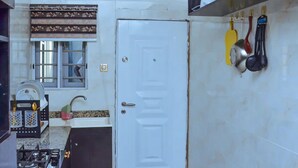 A kitchen with a white door, a window with a patterned curtain, and various kitchen utensils hanging on the wall. - D.T Homes Luxury Apartment (Ibadan)