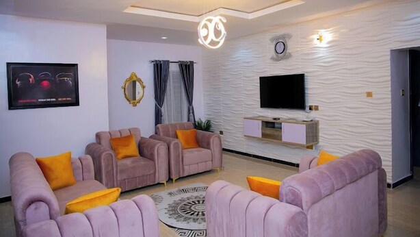 A modern living room with a flat-screen TV, a decorative mirror, and a patterned wall. - D.T Homes Luxury Apartment (Ibadan)