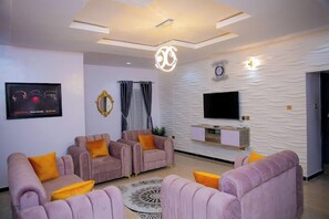 A modern living room with a flat-screen TV, a decorative mirror, and a patterned wall. - D.T Homes Luxury Apartment (Ibadan)