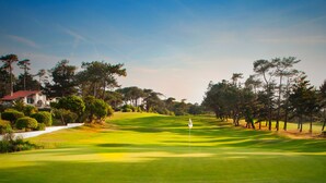 A golf course with a flagstick, surrounded by trees and a building with a red roof. - ACCOMMODATION RESIDENCE CHIBERTA AND GOLF WITH SWIMMING POOL (Anglet)