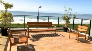 Eine Holzterrasse mit Bänken mit Blick auf einen Strand und das Meer.