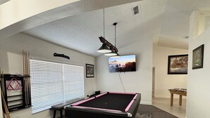 A pool table in a room with a ceiling fan, a window with blinds, and a framed picture on the wall. - Spacious 4-bedroom house in serene Deltona with AC, WiFi (Deltona)