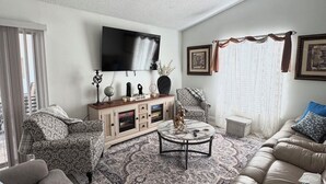 A living room with a ceiling fan, a flat-screen TV, a patterned rug, a sofa, and a coffee table. - Spacious 4-bedroom house in serene Deltona with AC, WiFi (Deltona)