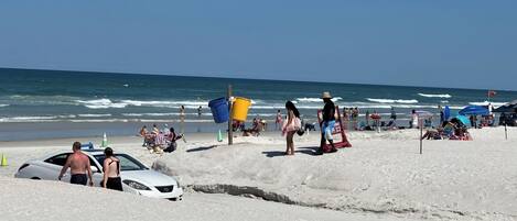 A beach with people, a lifeguard tower, and a white car.