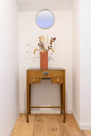 A wooden console table with a mirror above it, a vase with dried flowers, and a wooden floor.