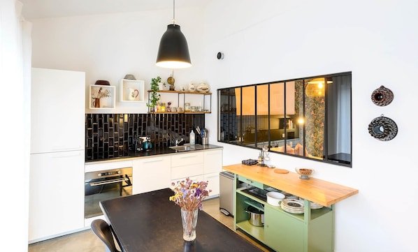A modern kitchen with a black pendant light, a wooden dining table, and a green cabinet.