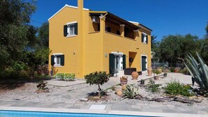 A two-story yellow house with a swimming pool in front.