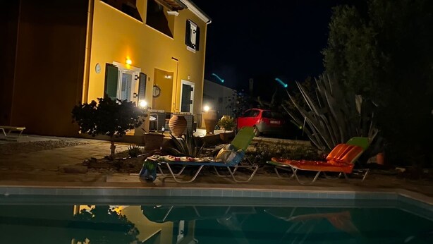 A nighttime view of a pool area with lounge chairs and a building in the background.