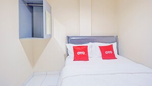 Un dormitorio con una cama, dos almohadas rojas con la marca 'OYO', un cabecero gris y una ventana pequeña con una barra de metal.