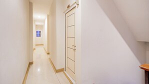 Un pasillo estrecho con una puerta a la derecha, un banco de madera y un suelo de baldosas.