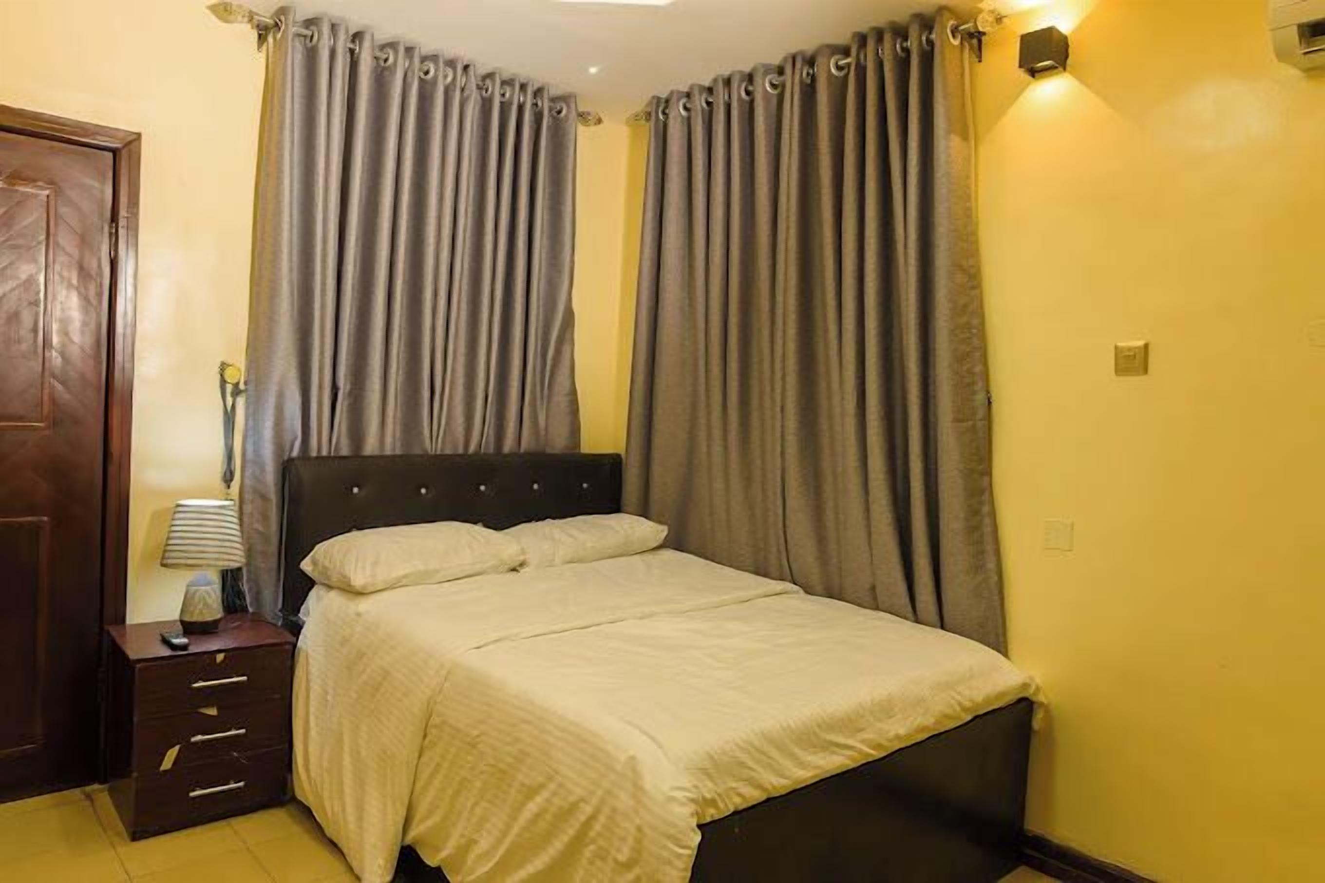 A bedroom with a bed, curtains, a nightstand, and a lamp.