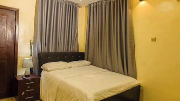 A bedroom with a bed, curtains, a nightstand, and a lamp.