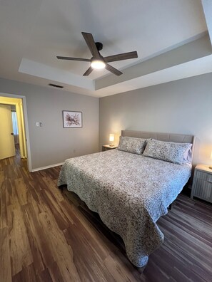 A bedroom with a large bed, a ceiling fan, a bedside table with a lamp, and a framed picture on the wall. - Charming 2-bedroom 2 bath duplex in the heart of Tyler! (Tyler)