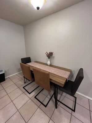 A dining area with a long table, two chairs, a vase with flowers, and a trash bin. - Charming 2-bedroom 2 bath duplex in the heart of Tyler! (Tyler)