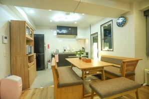 Un espacio habitable compacto con kitchenette, una mesa de comedor con bancos, un reloj en la pared y una pequeña zona de estar.