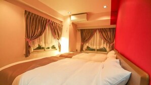 Una habitación de hotel con cama, cortinas, un equipo de aire acondicionado y una pared roja.