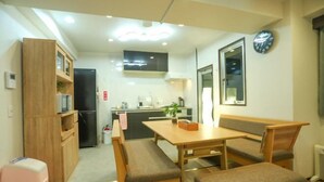 Un espacio habitable compacto con kitchenette, un área de comedor con bancos, un armario de madera y un reloj en la pared.