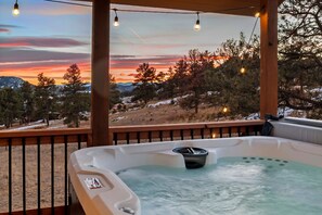 Un bain à remous offrant une vue sur un coucher de soleil se reflétant sur un paysage enneigé.