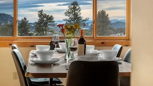 Mesa de comedor lista para cuatro personas, con platos blancos, vasos y un florero con flores.
