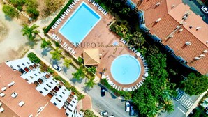 Vue aérienne d’un quartier résidentiel avec une piscine entourée de chaises longues et d’un espace salon abrité.