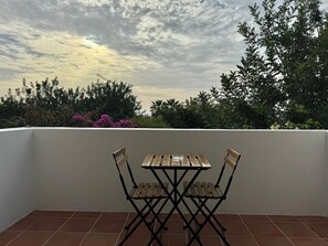 Una terraza con mesa y sillas de madera, rodeada por un muro blanco y un suelo de baldosas.