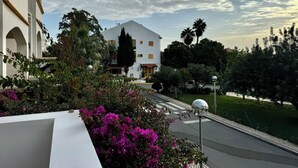 Un bâtiment blanc doté d’un balcon, entouré d’une végétation luxuriante et de fleurs violettes.