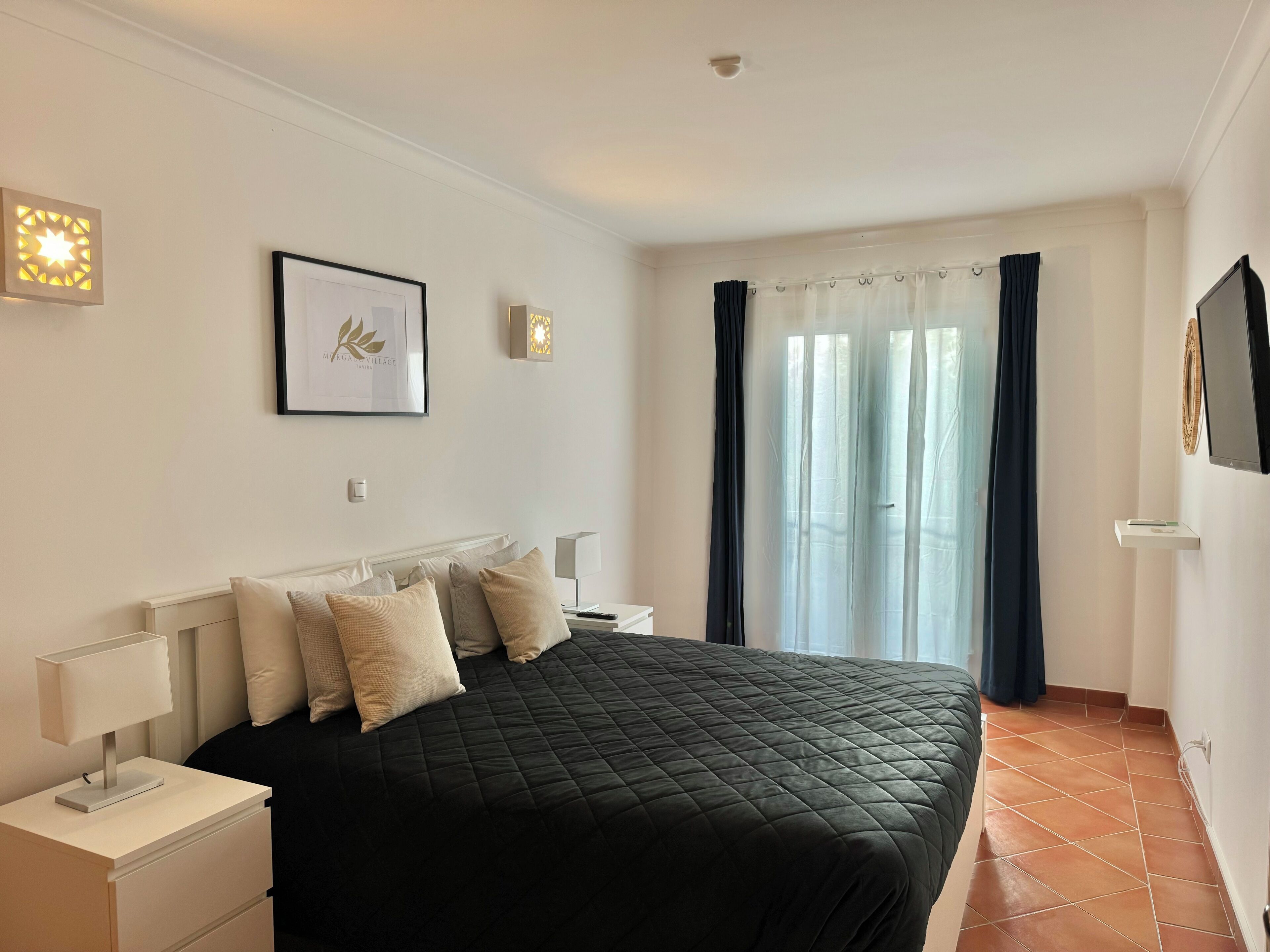 A bedroom with a bed, bedside tables, a framed picture, and a window with curtains.