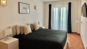 Une chambre à coucher avec un lit, des tables de chevet, un tableau encadré et une fenêtre avec des rideaux.