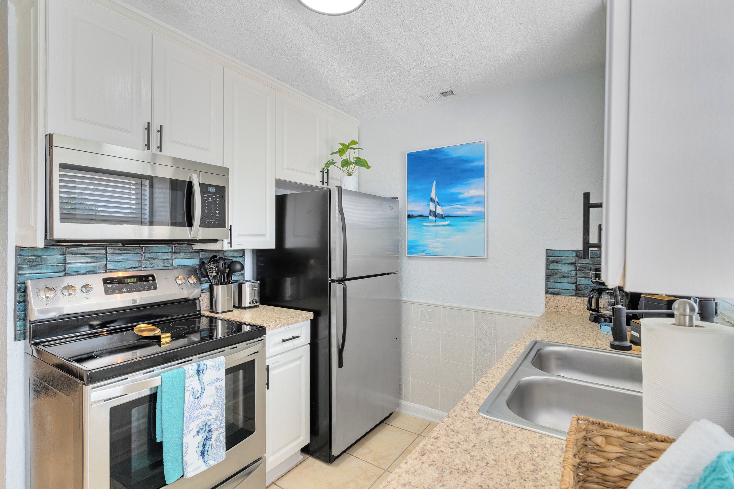 A modern kitchen with stainless steel appliances, white cabinetry, a tiled backsplash, and a painting of a sailboat on the wall.