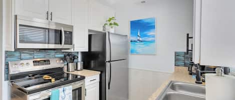 A modern kitchen with stainless steel appliances, white cabinetry, a tiled backsplash, and a painting of a sailboat on the wall.