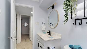 Un baño con lavamanos blanco, espejo, inodoro y toallero.