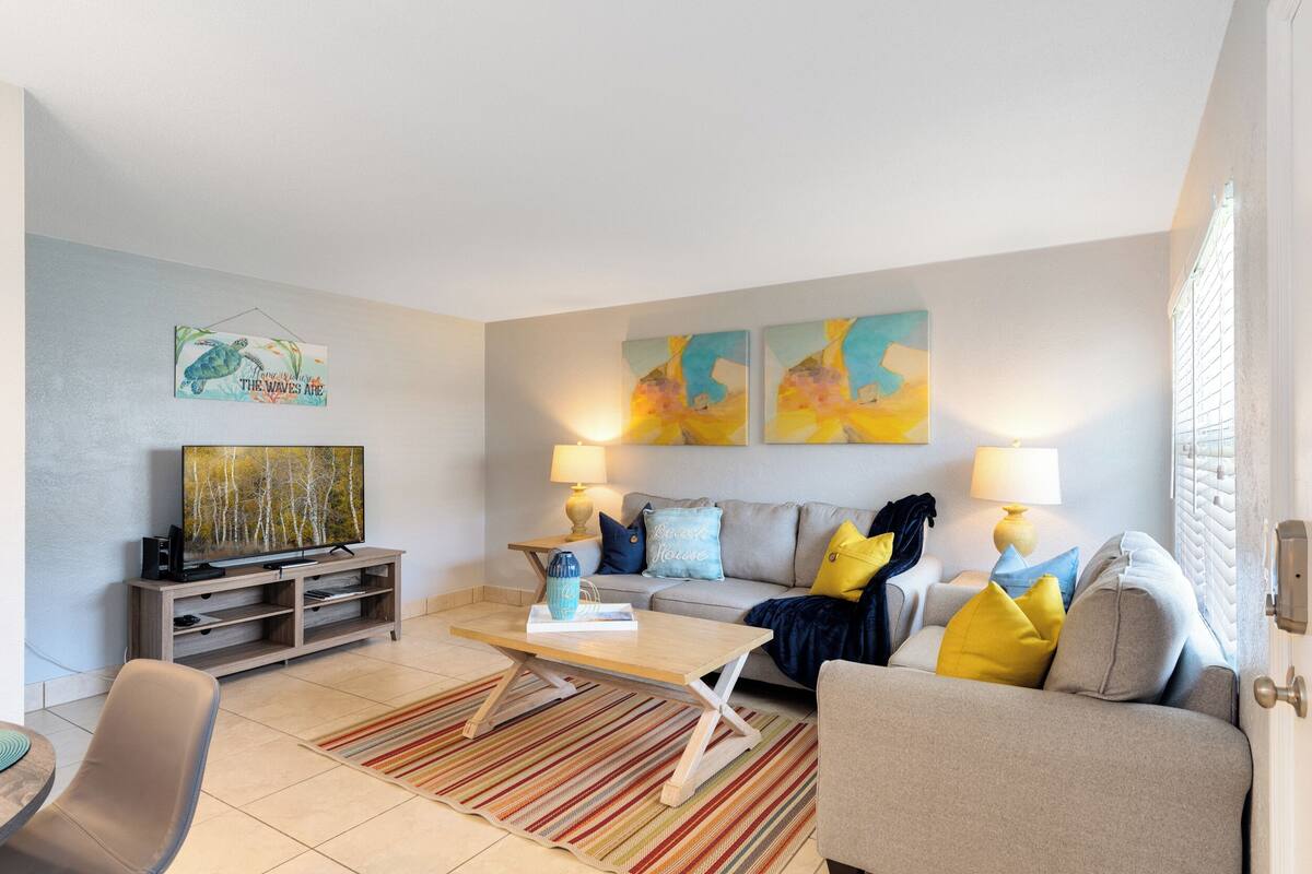 Una sala de estar con un sofá, una mesa de centro y un mueble para televisión. Hay dos lámparas a cada lado del sofá.