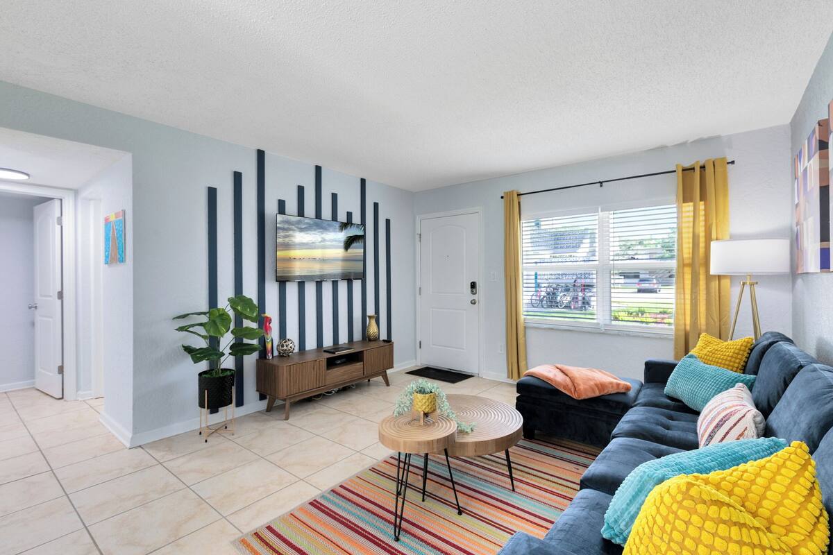 Una sala de estar moderna con un sofá, un televisor, una planta, una mesita y una ventana con cortinas.