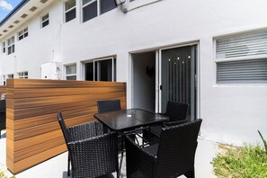 Un patio al aire libre con separador de madera, una mesa negra y sillas de mimbre negro.