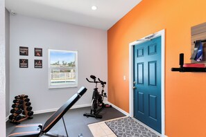 Un gimnasio en casa con una bicicleta estática, banco y mancuernas.