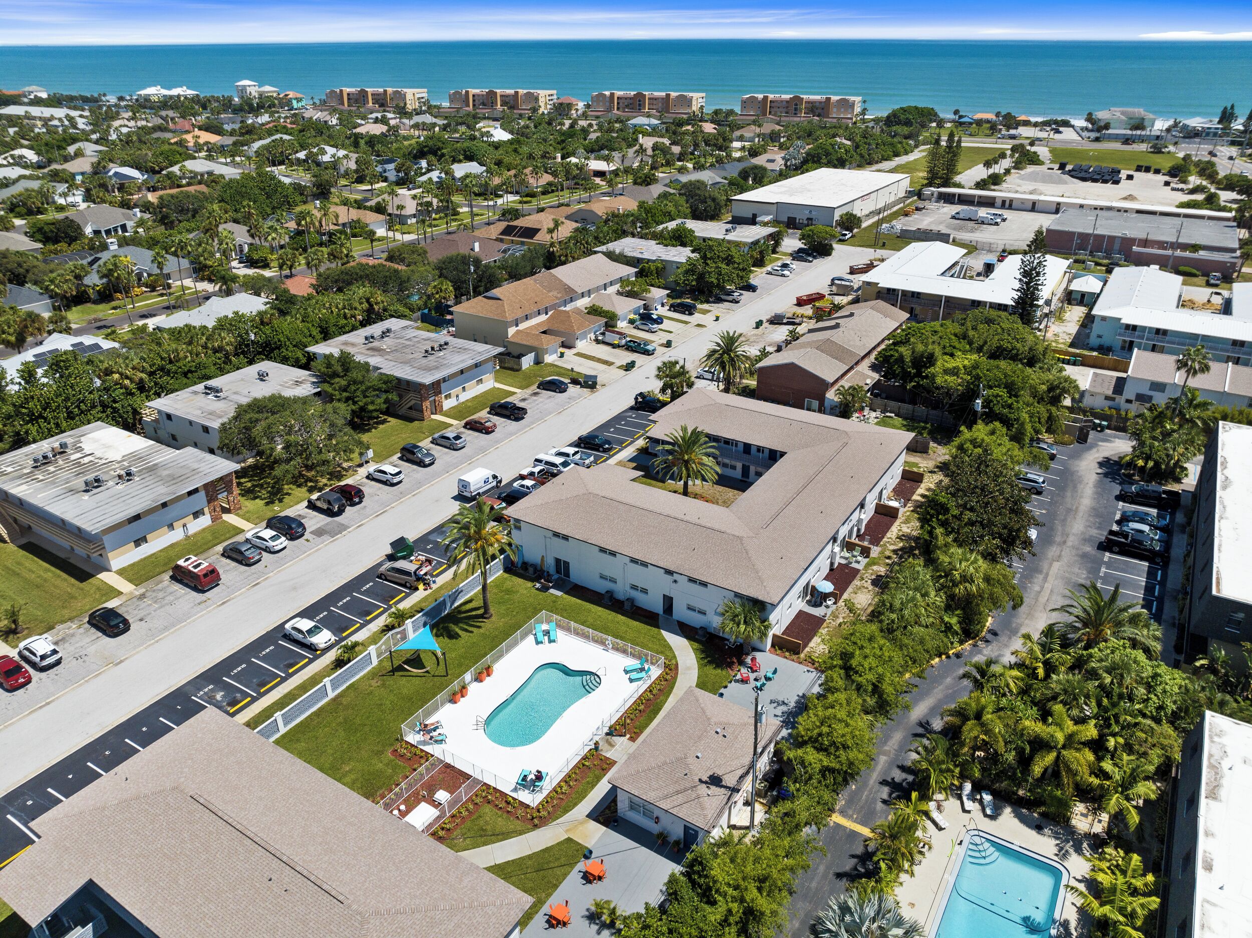 An aerial view of a residential area with a large building featuring a swimming pool and a parking lot.