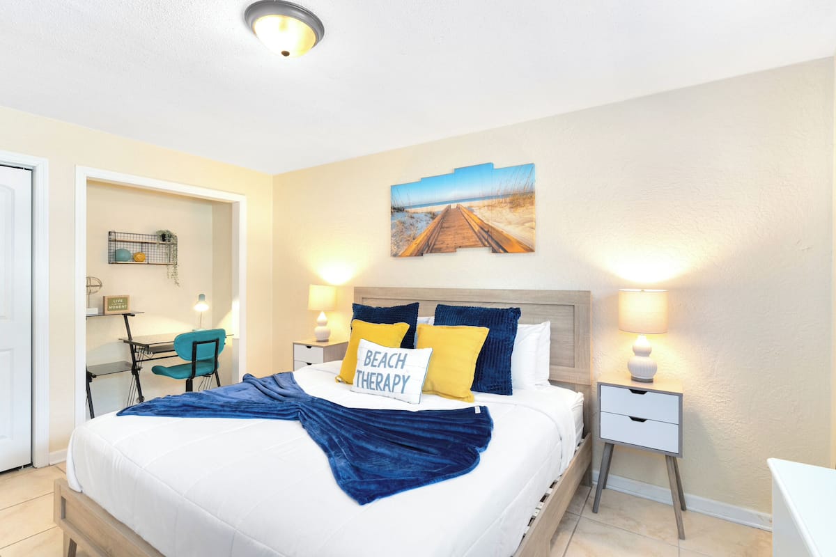 Un dormitorio ordenado con cama, mesitas de noche, escritorio y silla.