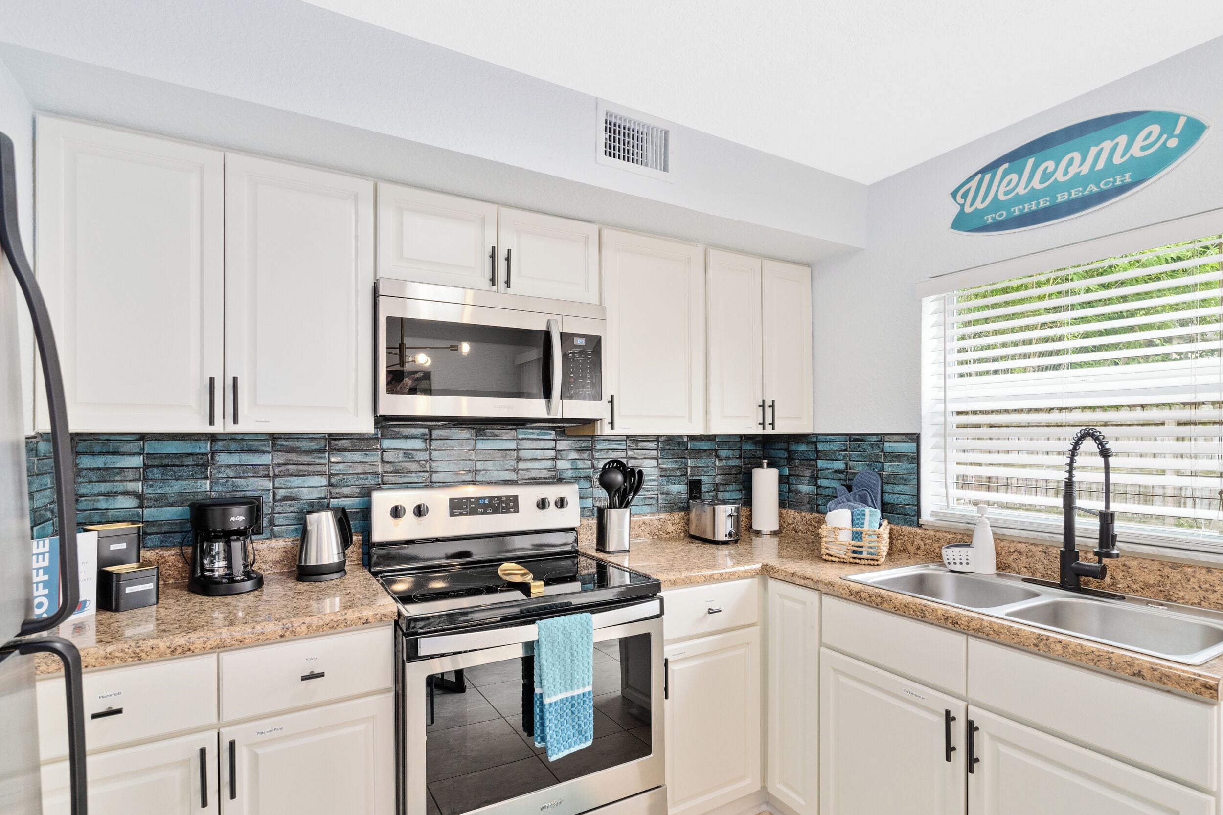 A modern kitchen with white cabinets, a stainless steel microwave, a stove, and a sink.