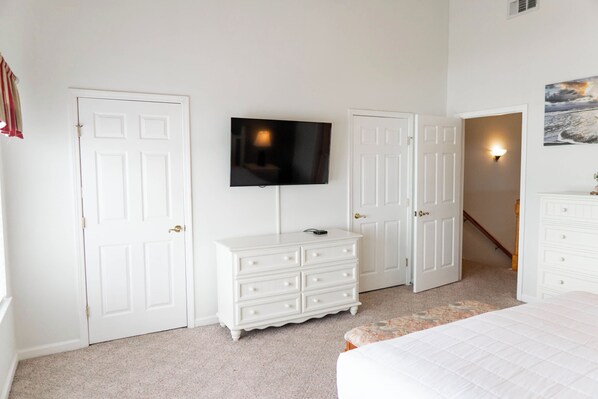 Un dormitorio con cama, cómoda, televisor y dos puertas.