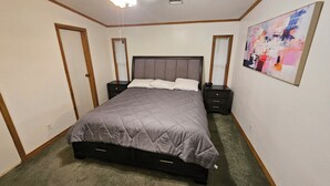 A bedroom with a large bed, two bedside tables, a ceiling fan, and a painting on the wall.