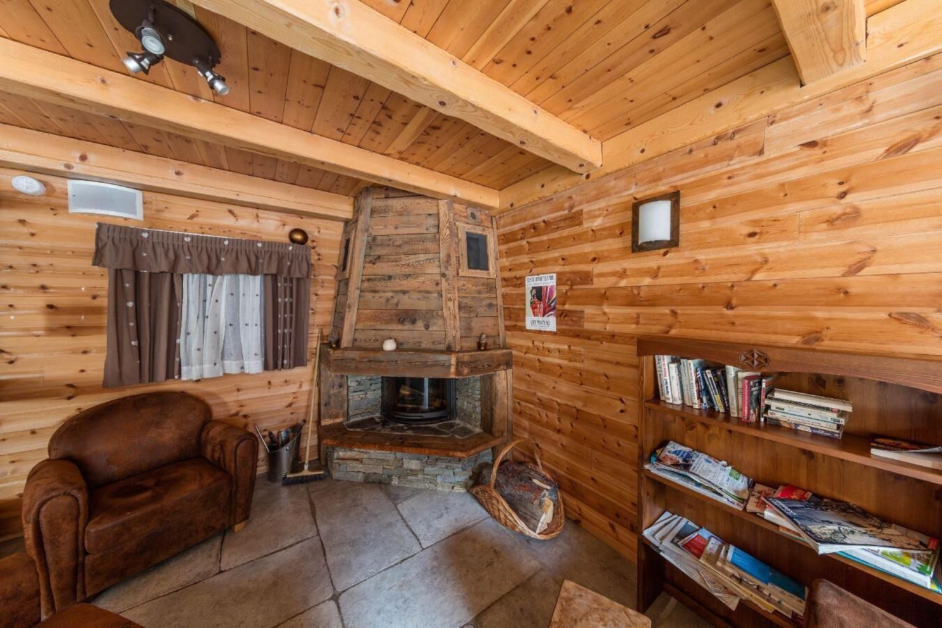 L’intérieur chaleureux d’un chalet avec une cheminée en pierre, des murs en bois, un fauteuil en cuir et une bibliothèque remplie de livres.