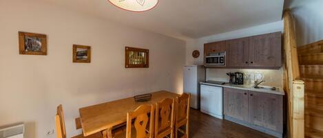 A compact kitchen with wooden cabinets, a dining table with chairs, and a hanging light fixture.