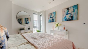 Un dormitorio con una cama grande, un espejo redondo, un aparador y pinturas abstractas en la pared.