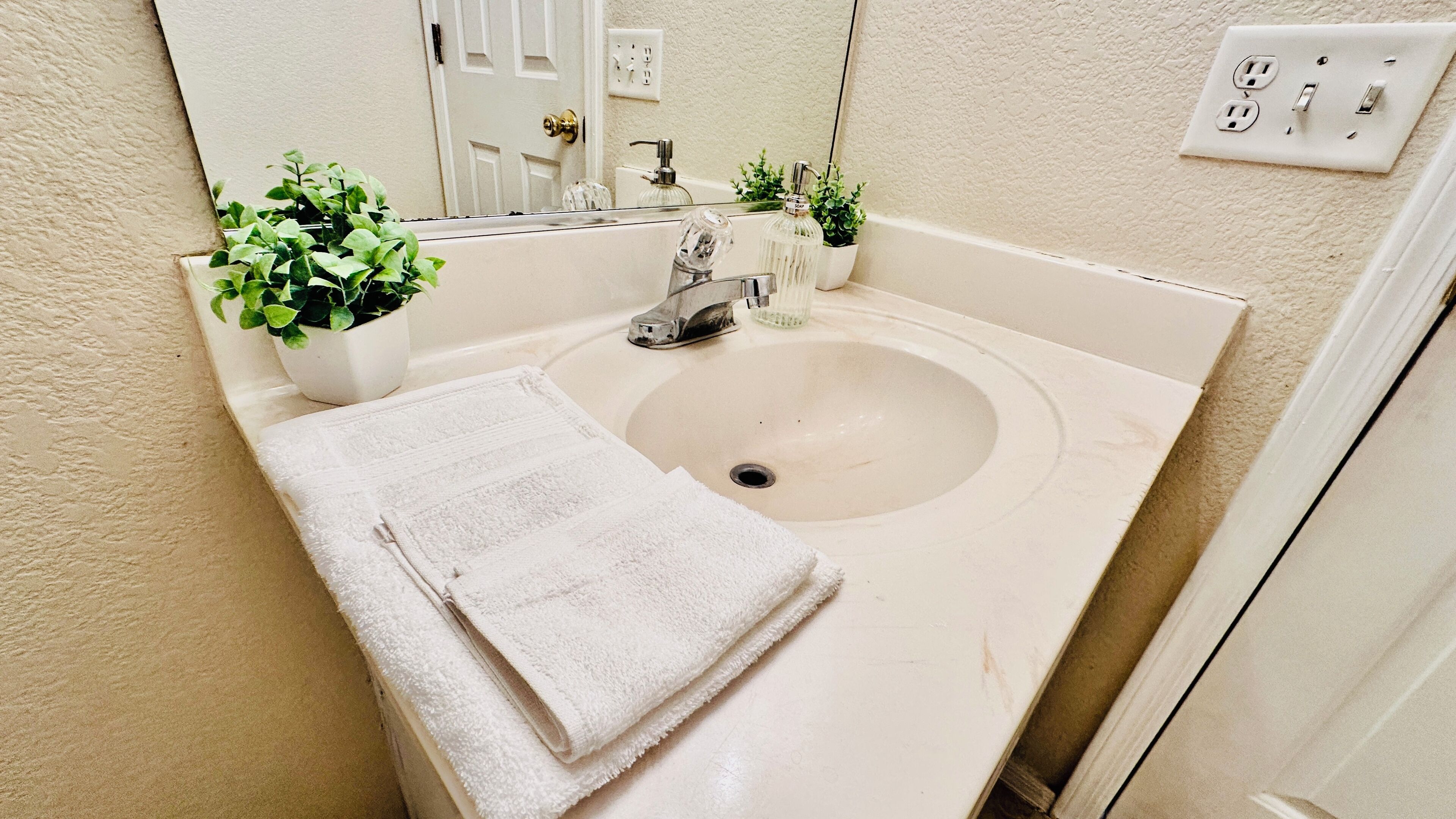 A bathroom with a sink, a mirror, a towel, and a potted plant.