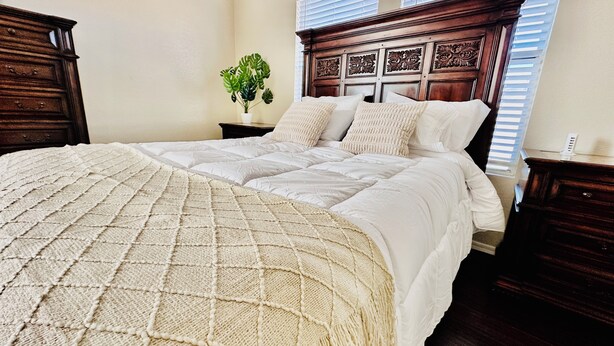 A neatly made bed with a quilted cover, a wooden headboard with decorative carvings, and a potted plant on the nightstand. - Tucson two story 4BR  2.5BA house close to airport & major attractions Sleeps 8 (Tucson)