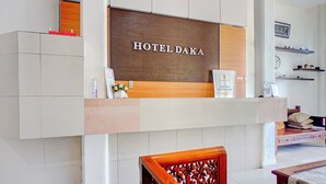 Un espace d’accueil avec une enseigne indiquant « HÔTEL DAKA », un comptoir de réception et une chaise en bois.