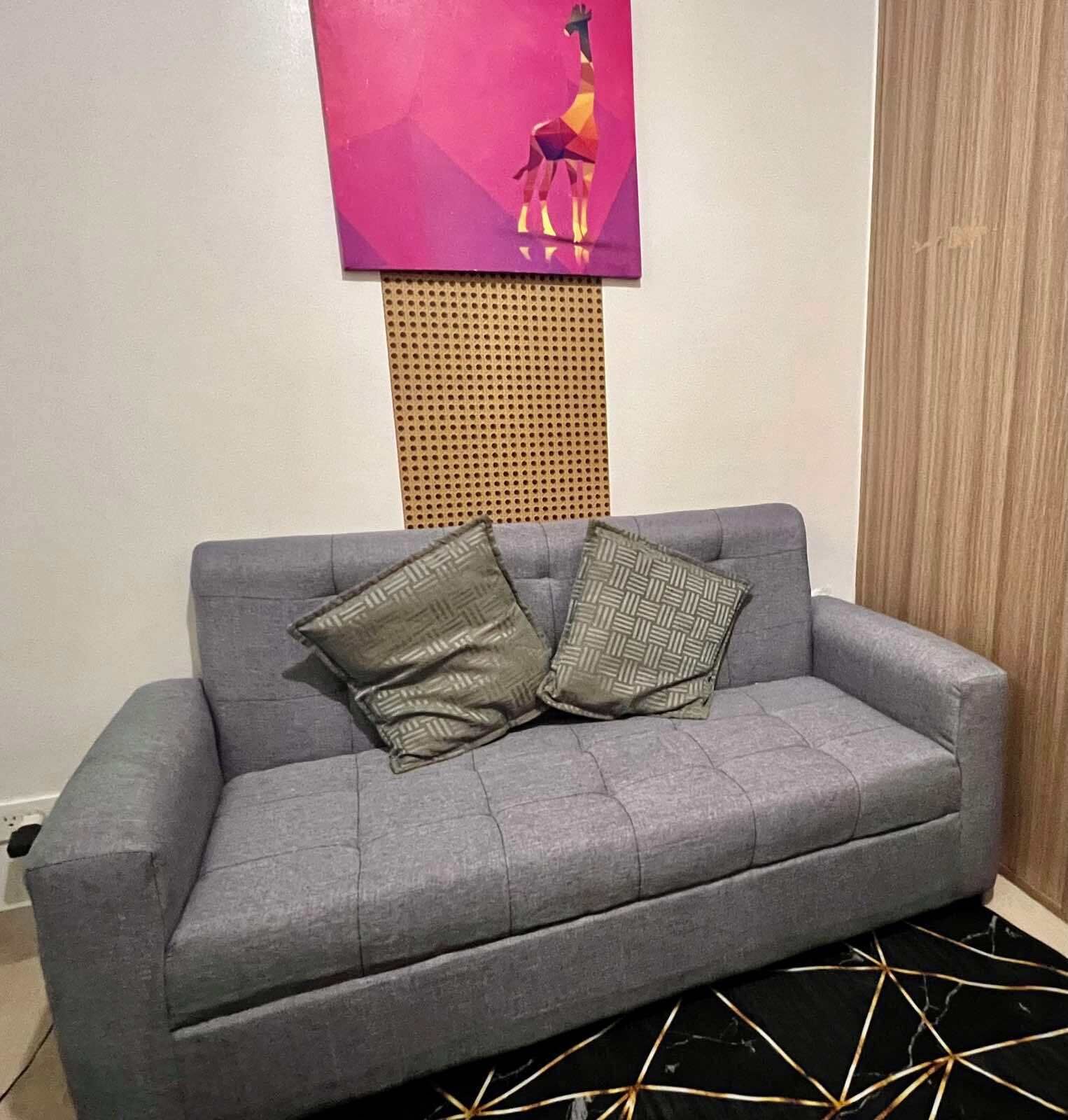 A grey sofa with two patterned cushions, a wall-mounted artwork of a giraffe, and a perforated panel above the sofa.