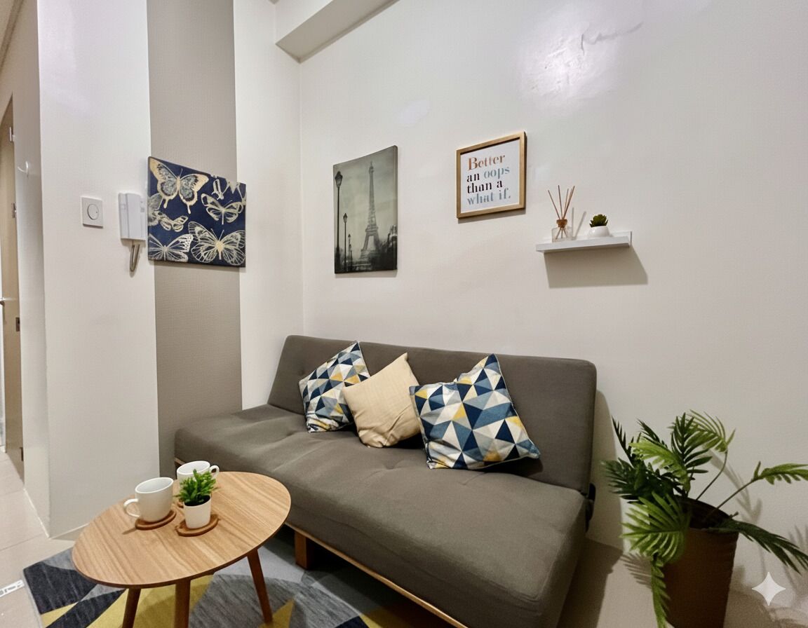 Ein modernes Wohnzimmer mit einem grauen Sofa, gemusterten Kissen, einem kleinen Holztisch mit zwei Tassen und einer Pflanze, sowie Wandbildern, darunter ein gerahmtes Zitat und ein Bild des Eiffelturms.