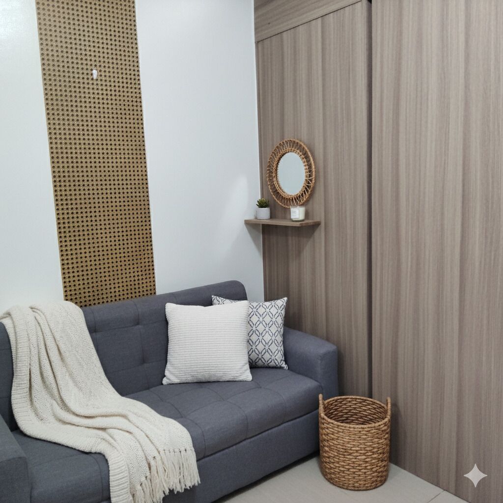 Un divano grigio con una coperta bianca e cuscini decorati, un cesto di vimini e una mensola a parete con uno specchio e una piccola pianta.