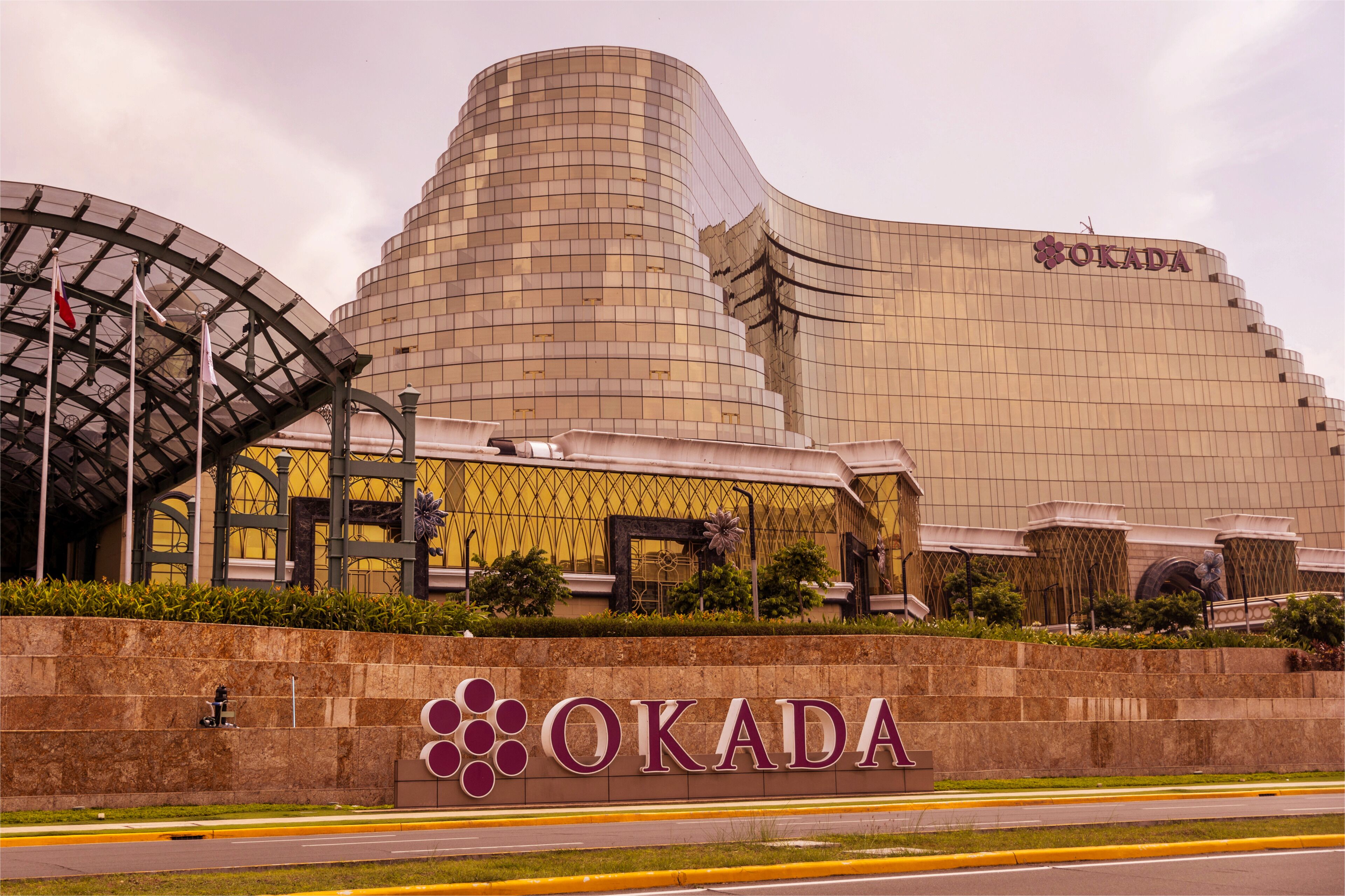 Un grand bâtiment moderne dont la façade porte en lettres bien visibles l’inscription « OKADA ».